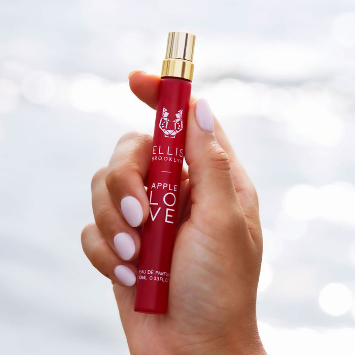 Model with light pink nail polish holding Apple Love 10ml Eau De Parfum Travel Spray against white background.