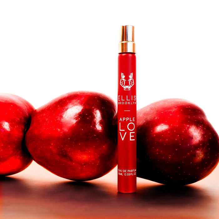 Apple Love 10ml Eau De Parfum Travel Spray on white table in front of apples, against white background.