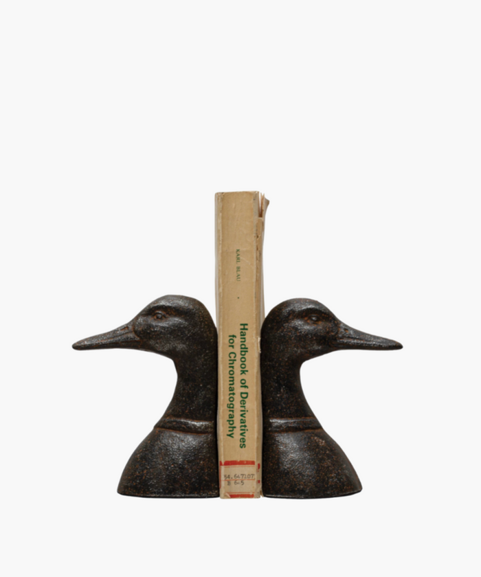 Two bronze duck head bookends face opposite directions with a book in the middle against a white background. They feature detailed textures, conveying a classic and elegant tone. | SW Home