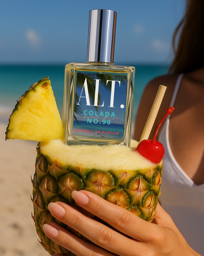 ALT. Fragrances Colada Perfume in a Pina Colada Drink on the beach being held by a woman.