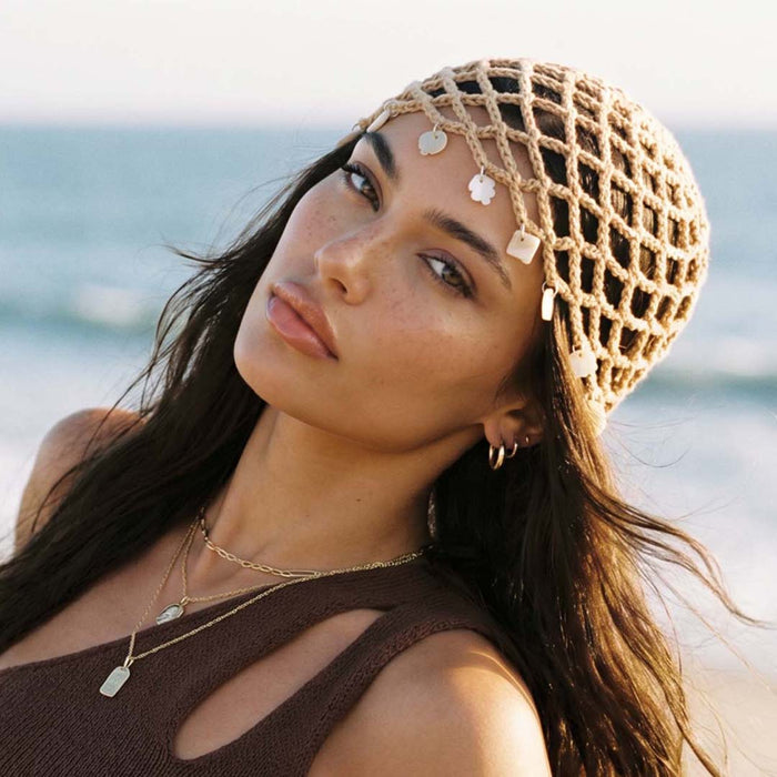 Coastal-inspired crochet beanie with shell charms for beachwear and resort looks.