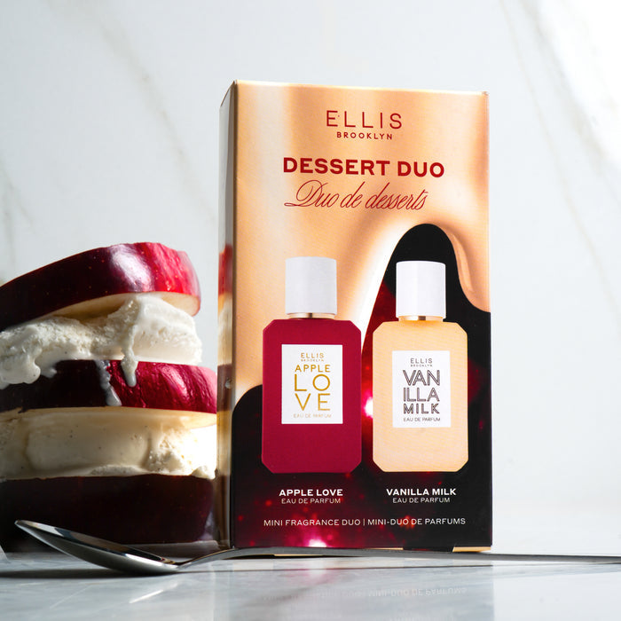 Dessert Duo box standing next to sliced red apple and vanilla ice cream stacked on one another, behind spoon, on marble background.
