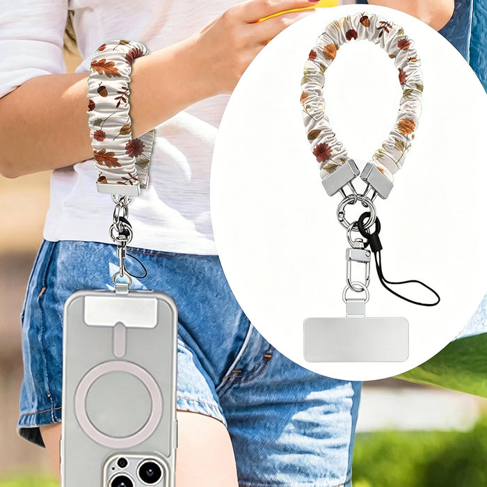 Fall Floral Bliss scrunchie phone wrist strap worn on the wrist with a phone in a clear MagSafe case, with an inset close-up of the cream floral strap, silver clasp, and attachment tab.