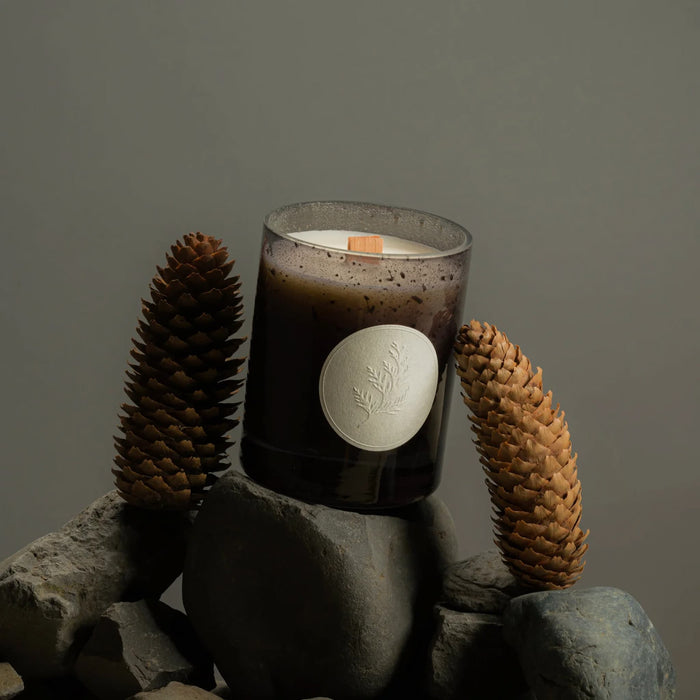 Fischersund Jol holiday candle in a textured glass container with pine cones on rocks against a dark background