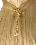 Back view of a model wearing a gold Tinkerbell hair hook with dangling clear bead charms securing a ponytail.