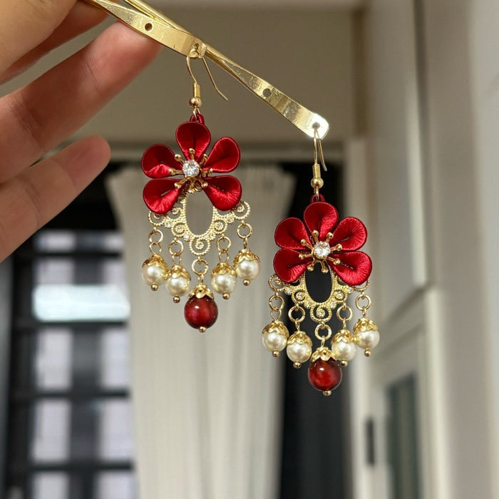 Chanhua handmade red flower drop earrings with gold filigree teardrop frame, four pearl drops, and one deep red stone drop on gold chains, held up against a white interior background