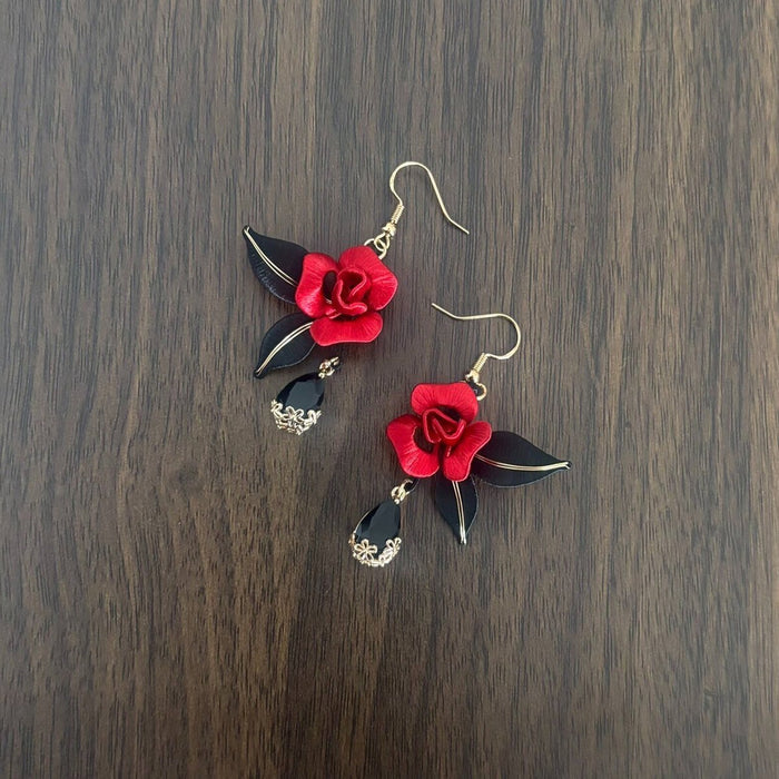 Handcrafted Chanhua thread-wrapped earrings featuring a blooming red rose with black leaves and black teardrop dangles on a wooden background.
