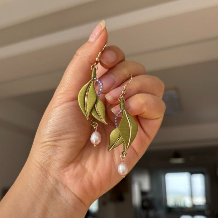 Handheld view of handmade Chanhua thread-wrapped earrings featuring elegant green leaves, purple bead accents, and pearl drops.