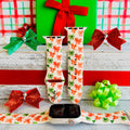 Jingle Bows Apple Watch band with red, orange, and green ribbon bows on cream background styled with wrapped Christmas presents