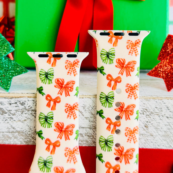 Jingle Bows Apple Watch band with red, orange, and green ribbon bows on cream background styled with wrapped Christmas presents