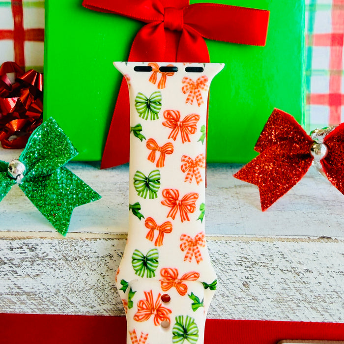 Jingle Bows Apple Watch band with red, orange, and green ribbon bows on cream background styled with wrapped Christmas presents