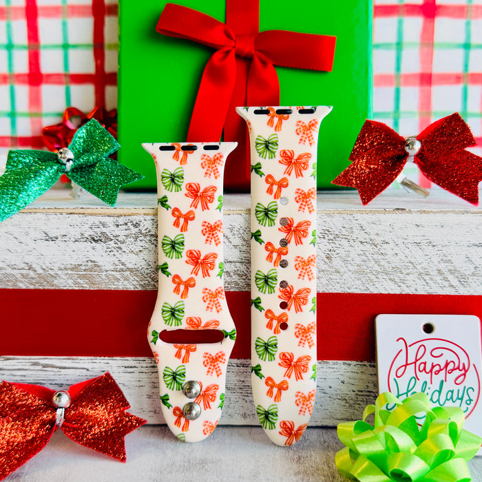 Jingle Bows Apple Watch band with red, orange, and green ribbon bows on cream background styled with wrapped Christmas presents