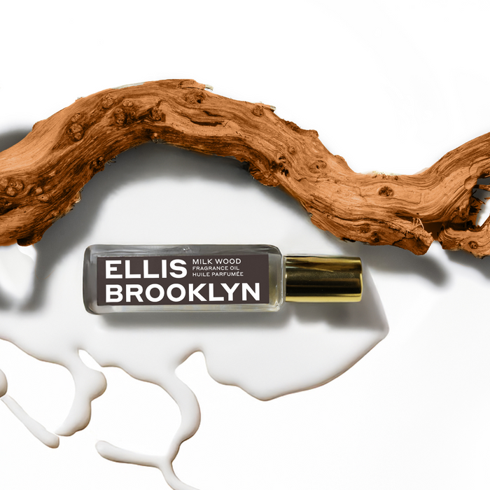 Milk Wood Fragrance Oil 15ml resting in milk next to piece of wood on white background.