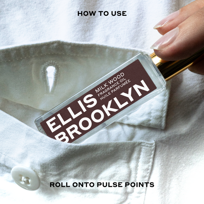 Model wearing white button-down shirt placing Milk Wood Fragrance Oil 15ml into shirt pocket between black text that reads "How To Use Roll Onto Pulse Points".