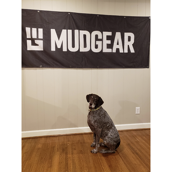 MudGear race banner 3x8 feet displayed on wall above brown dog sitting on wooden floor