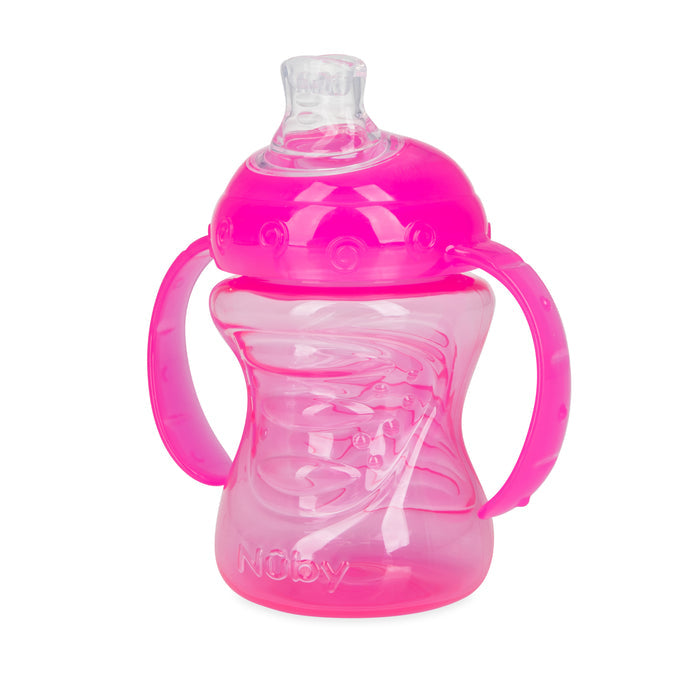 The Nuby No-Spill Soft Spout Grip N' Sip Trainer Cup is a pink plastic cup for young children, featuring two side handles, a clear silicone spout, and leak-resistant design. "Nuby" is embossed on the front.