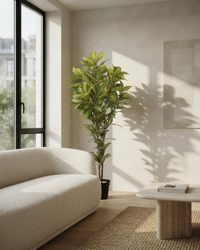 Tall artificial green plant in black pot near sofa, indoor corner view