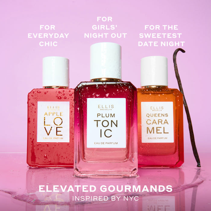 APPLE LOVE Eau de Parfum 50ml, PLUM TONIC Eau de Parfum 50ml, and QUEENS CARAMEL Eau de Parfum 50ml covered in water droplets next to vanilla bean and on top of water puddle on pink background with white text that reads "For Everyday Chic. For Girls' Night Out. For The Sweetest Date Night. Elevated Gourmands Inspired by NYC"