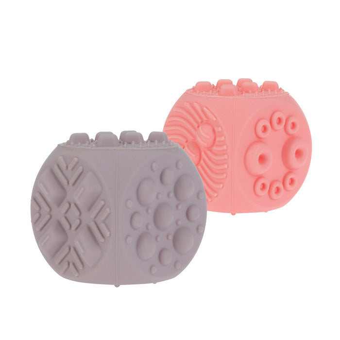 The Nuby US Silicone Popper Blocks (2 Pack) in lavender and pink feature raised geometric patterns and are set against a white background—ideal sensory toys for babies to help develop fine motor skills.