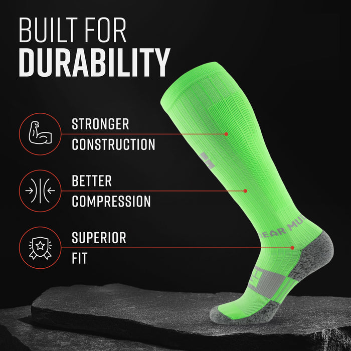 Neon green tall compression sock with gray heel and toe, displayed on dark stone surface