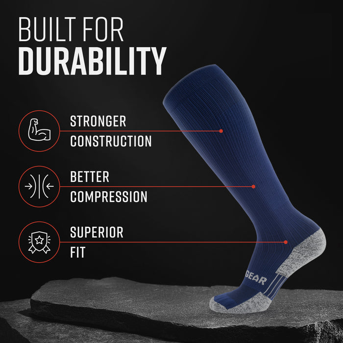 Navy tall compression sock with gray heel and toe, displayed on stone with durability features highlighted